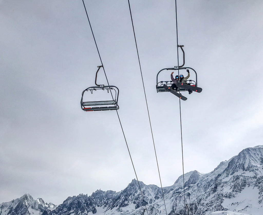 Happy skiers on lift wavintg overhead.